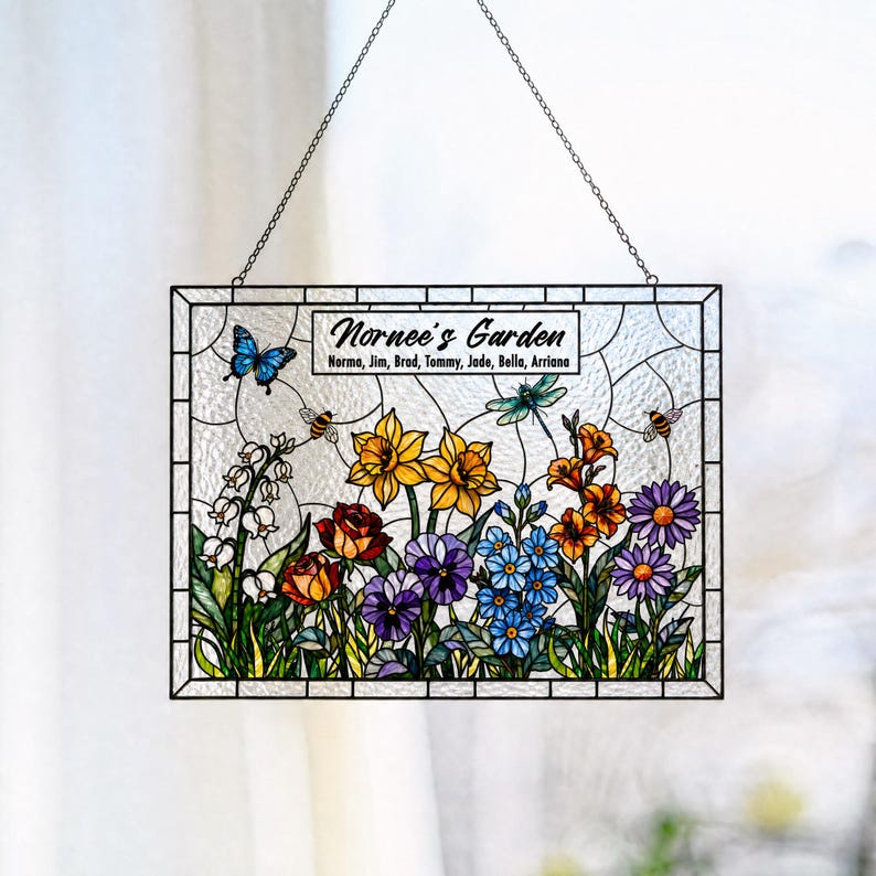 May include: A rectangular stained glass suncatcher featuring a garden scene with colorful flowers, a blue butterfly, a dragonfly, and bees. The text reads Nornee's Garden followed by the names Norma, Jim, Brad, Tommy, Jade, Bella, and Arriana.