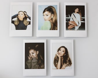 May include: Five Polaroid photos of a woman with long brown hair. The photos are arranged in a grid pattern on a white wall. The woman is wearing different outfits in each photo.
