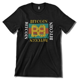 Puede incluir: Camiseta negra con un diseño gráfico de estilo vintage que presenta la palabra "Bitcoin" repetida alrededor de un logotipo "B" estilizado en amarillo y dorado.