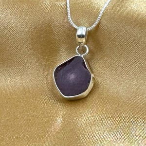 Puede incluir: Un collar de cadena de plata con un colgante con una piedra de color púrpura de forma irregular.
