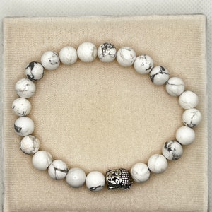 May include: White Howlite beaded bracelet with a silver Buddha charm.