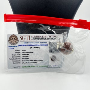 May include: A brown Rudraksha pendant with a 5-Mukhi certification card. The card includes details like weight, shape, and origin. The card is issued by Surbhi Gems Testing.