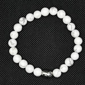 May include: White gemstone bracelet with a silver charm. The bracelet is made of round white beads and has a silver charm with a design on it.