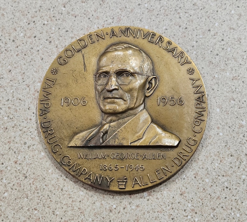 May include: A bronze commemorative medal celebrating the 50th anniversary of the Tampa Drug Company, founded in 1906. The medal features a portrait of William George Allen, the company's founder, and the text "Golden Anniversary" and "Tampa Drug Company Allen Drug Company 1906-1956".
