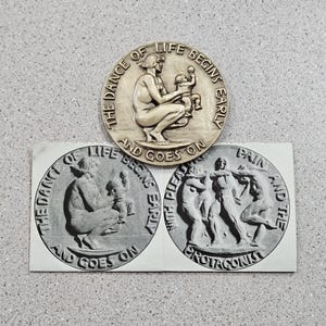 May include: A collection of three circular relief sculptures. The top sculpture depicts a woman holding a baby, with the text "THE DANCE OF LIFE BEGINS EARLY AND GOES ON." The other two sculptures are similar.