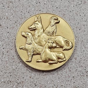 May include: A gold-colored metal medal featuring three dogs in relief. The dogs are a German Shepherd, a Poodle, and a Beagle.
