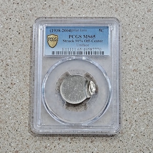 May include: A silver coin graded PCGS MS65, struck 90% off-center, with a uniface. The coin is encased in a clear plastic holder with a black label that reads "(1938-2004) Mint Error", "PCGS MS65", "Struck 90% Off-Center", "Uniface", and "E11111.65/49587770".