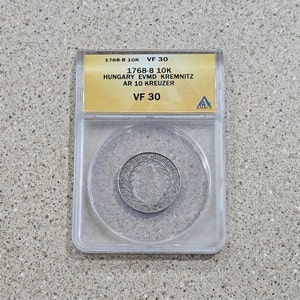 May include: A silver coin from 1768-B, graded VF 30 by ANACS, from Hungary, with the inscription "EVMD KREMNITZ AR 10 KREUZER".