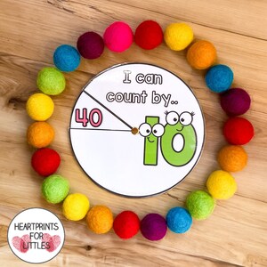 May include: A colorful felt ball garland surrounds a white circular spinner with the text "I can count by..." and a large green number 10 with googly eyes. The spinner also has a pink number 40.