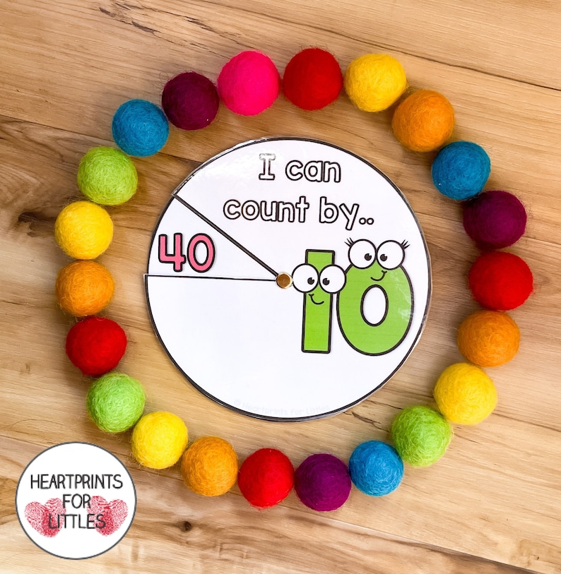 May include: A colorful felt ball garland surrounds a white circular spinner with the text "I can count by..." and a large green number 10 with googly eyes. The spinner also has a pink number 40.