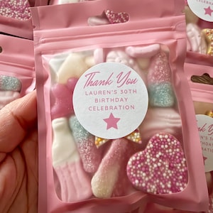 Peut inclure: Sacs roses en cellophane remplis de bonbons assortis. Chaque sac porte un autocollant avec l'inscription "Thank You, Lauren's 30th Birthday Celebration" et une étoile rose. Les bonbons sont roses, blancs et bleus.