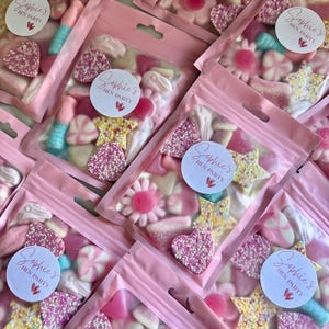 Puede incluir: Primer plano de bolsas rosas de celof&aacute;n llenas de caramelos variados. Los caramelos, en tonos rosa, blanco y azul, incluyen corazones, estrellas y flores. Cada bolsa tiene una etiqueta que dice "Sophie's Hen Party".