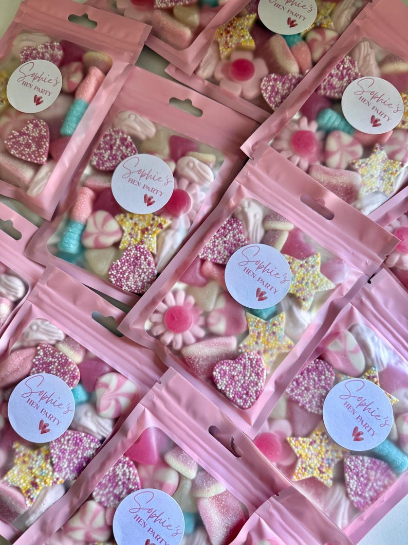 Puede incluir: Primer plano de bolsas rosas de celof&aacute;n llenas de caramelos variados. Los caramelos, en tonos rosa, blanco y azul, incluyen corazones, estrellas y flores. Cada bolsa tiene una etiqueta que dice "Sophie's Hen Party".