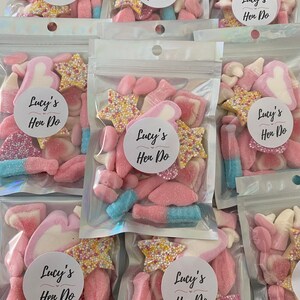 Peut inclure: Plusieurs sachets transparents remplis de bonbons roses, blancs et bleus. Chaque sachet porte un autocollant rond avec l'inscription "Lucy's Hen Do". Les bonbons comprennent des &eacute;toiles saupoudr&eacute;es et des guimauves.