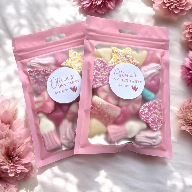 Puede incluir: Dos bolsas rosas de celof&aacute;n llenas de caramelos variados. Cada bolsa tiene una pegatina redonda que dice "Olivia's HEN PARTY" y la fecha "21.02.2020". Los caramelos son rosas, blancos y amarillos, con forma de estrella y coraz&oacute;n.