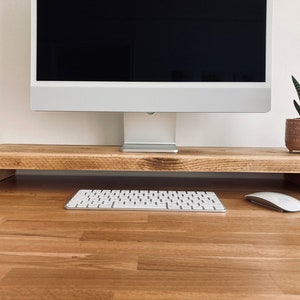 Pu&ograve; includere: Un supporto per monitor in legno con una tastiera bianca e un mouse bianco su una scrivania in legno. Una pianta grassa in vaso &egrave; sulla scrivania dietro il supporto.
