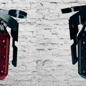 May include: Two stylized, metallic grenade replicas. One is a vibrant red, the other is black. Both have a detailed design with a lever and pin. The background is a white brick wall.