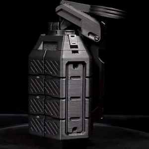 May include: A black, 3D-printed grenade keychain. The keychain features a detailed design with a pin, lever, and segmented body. The background is black, highlighting the object's shape and texture.