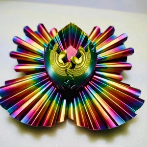 May include: A rainbow iridescent metal sculpture with a geometric design. The sculpture is made of multiple pieces that fit together to create a unique and intricate design.