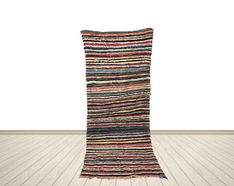 Op de afbeelding: Een rechthoekig tapijt met horizontale strepen in verschillende kleuren, waaronder rood, blauw, bruin en beige. Het tapijt heeft een textuur en een gefranjerde rand. Het tapijt wordt tegen een witte achtergrond gepresenteerd.