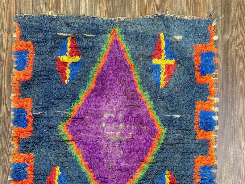 a vibrant, colorful rug with a diamond pattern in shades of purple, blue, and orange.