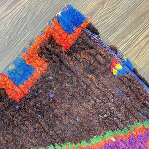 a close-up view of a colorful, textured rug with a mix of brown, orange, blue, and purple hues. The rug appears to be made of wool and has a distinctive, intricate design.