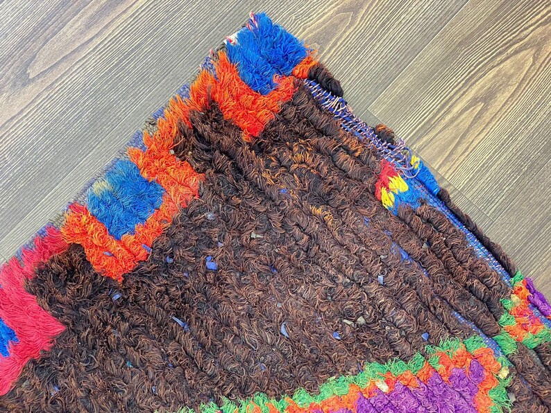 a close-up view of a colorful, textured rug with a mix of brown, orange, blue, and purple hues. The rug appears to be made of wool and has a distinctive, intricate design.