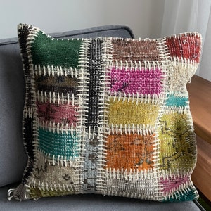 May include: A patchwork cushion featuring a mix of colours and textures, including green, brown, pink, yellow, and blue. The cushion is crafted from various fabrics stitched together with white thread.