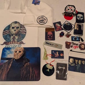 May include: A collection of Friday the 13th merchandise including a white tote bag with a Jason for President graphic, a white beanie with a Camp Crystal Lake patch, a mousepad, stickers, a bookmark, a zipper pouch, and various pins and patches.