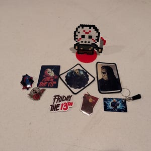 May include: A collection of Friday the 13th themed items including a pixel art figure of a hockey-masked character, several stickers featuring the movie title and character imagery, a rectangular patch, and a keychain with a small black tassel.