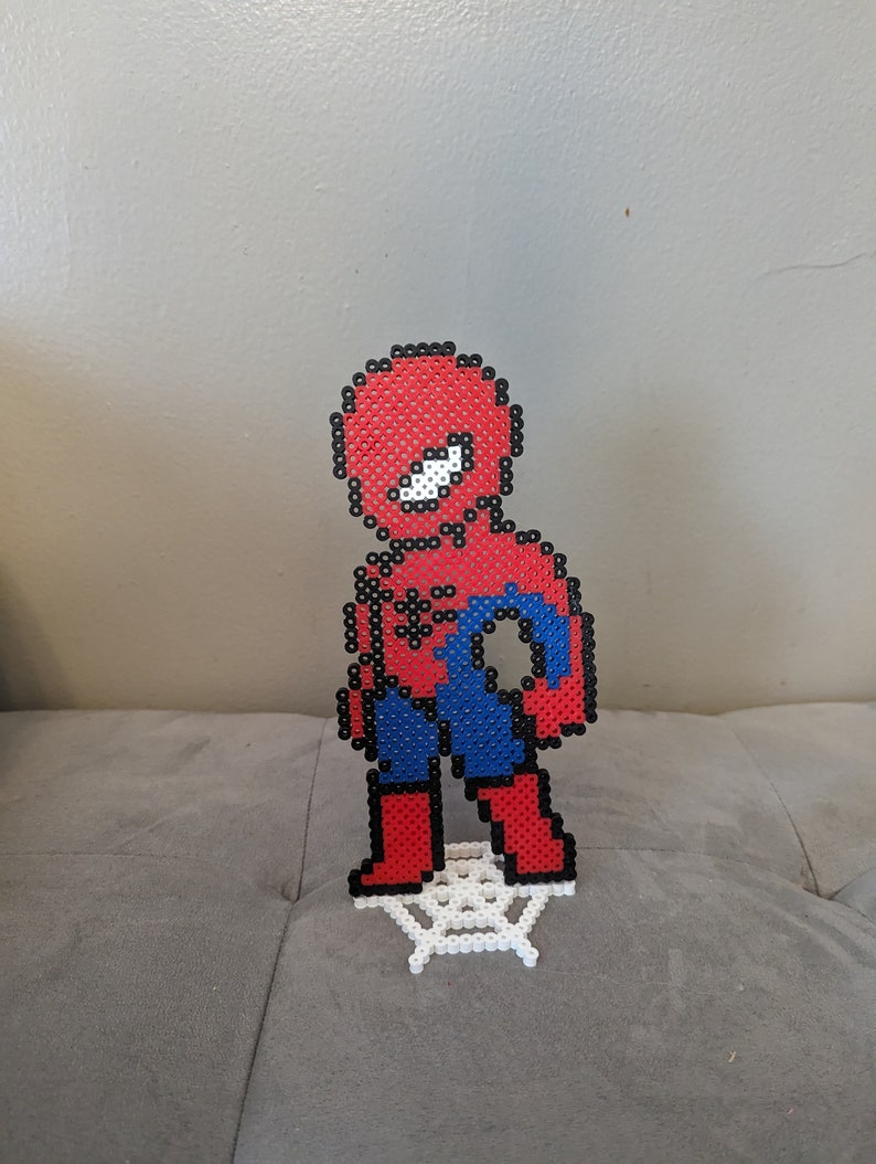 Puede incluir: Una figura de pixel art roja y azul de Spider-Man de pie sobre una telara&ntilde;a de pixel art blanca.