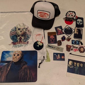 May include: A collection of Friday the 13th themed merchandise including a white drawstring bag with a Jason for President graphic, a black and white Camp Crystal Lake trucker hat, a mousepad, a zippered pouch, stickers, and various small accessories.