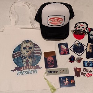 May include: A collection of horror-themed merchandise including a white tote bag with a Jason Voorhees graphic, a black and white Camp Crystal Lake trucker hat, various stickers, patches, a bookmark with a tassel, and a pixel art figure.