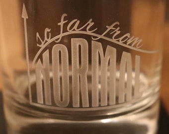 May include: A clear glass with the text "so far from NORMAL" etched on the side. The text is in a stylized font and is curved to resemble a graph.
