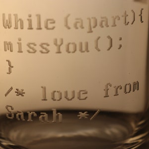 Pode incluir: Um copo de vidro transparente com o texto "While (apart){ missYou(); } /* love from Sarah */" gravado nele.