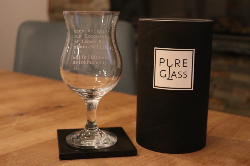 K&ouml;nnte beinhalten: Ein klares Glas mit Stiel und einer breiten Schale, graviert mit einem humorvollen Code-Snippet. Das Glas steht auf einem schwarzen Untersetzer. Das Glas ist in einer schwarzen Box verpackt, auf der "PURE GLASS" steht.