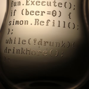 K&ouml;nnte beinhalten: Ein klares Glas mit einem humorvollen Code, der in die Seite graviert ist. Der Code lautet: "beer.Drink(); fun.Execute(); if (beer=0) { simon.Refill(); } while(!drunk) { drinkMore(); }"