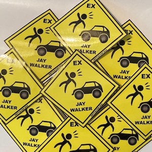 May include: A collection of yellow stickers with a black car and a person being hit by the car graphic. The stickers have the text "EX" and "JAY WALKER" printed on them. The website "UNITY16.COM 2024" is also printed on the stickers.