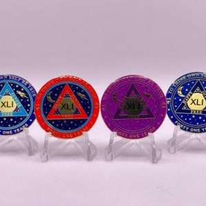 May include: Four round, gold-colored coins with a blue, red, purple, and blue background. Each coin features a triangle with the number "XLI" inside. The text "41 TO THINE OWN SELF BE TRUE 41" is around the edge of each coin. The coins are on small, clear stands.