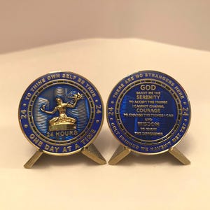 May include: Two blue and gold medallions with text and a figure. One reads "TO THINE OWN SELF BE TRUE" and "ONE DAY AT A TIME." The other says "GOD GRANT ME THE SERENITY." Both are on small stands.
