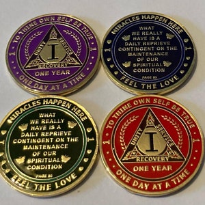 May include: Four gold-colored recovery coins with different colored rims: purple, blue, green, and red. Each coin has text including "Recovery", "One Year", and "One Day at a Time". The blue and green coins have the text "Miracles Happen Here".