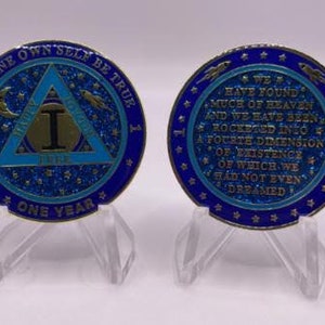 May include: Two blue and gold commemorative coins with a triangle design and the text "To thine own self be true" and "One Year". The back of the coin has the text "We have found much of heaven and we have been rocketed into a fourth dimension of existence of which we had not even dreamed."