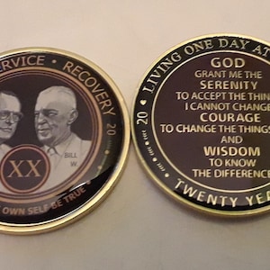 May include: Two gold-colored commemorative coins. One coin features portraits of two men and the text "Unity Service Recovery" and "To Thine Own Self Be True". The other coin has the text "God grant me the serenity" and "Twenty Years".