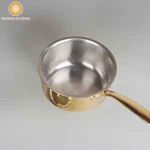 Könnte beinhalten: Ein goldfarbener, gehämmerter Edelstahltopf mit silbernem Innenraum und einem langen Griff.