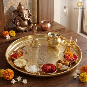May include: A golden brass puja thali with a lit candle, small bowls of spices and nuts, a bell, and red roses. The thali is round and has an engraved design.