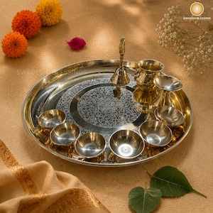 May include: A golden brass puja thali with a lit candle, small bowls of spices and nuts, a bell, and red roses. The thali is round and has an engraved design.