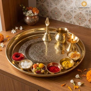 May include: A golden brass puja thali with a lit candle, small bowls of spices and nuts, a bell, and red roses. The thali is round and has an engraved design.