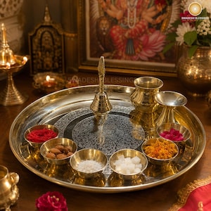 May include: A golden brass puja thali with a lit candle, small bowls of spices and nuts, a bell, and red roses. The thali is round and has an engraved design.