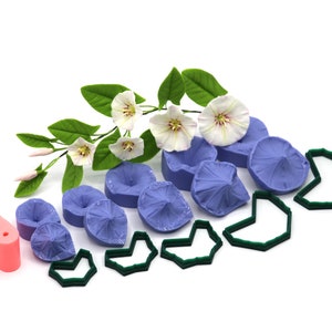 May include: A set of silicone molds for making polymer clay flowers. The molds are in the shape of morning glory flowers and leaves. There are also green cutters for shaping the clay. The molds are purple and the cutters are green.