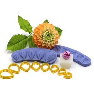 Könnte beinhalten: Ein Set aus Silikonformen und Ausstechern zum Herstellen von Polymer Clay Blumen. Die Formen sind lila und haben Blattformen. Die Ausstecher sind gelb und haben die Form von Blütenblättern. Eine kleine rosa Blume ist ebenfalls enthalten.